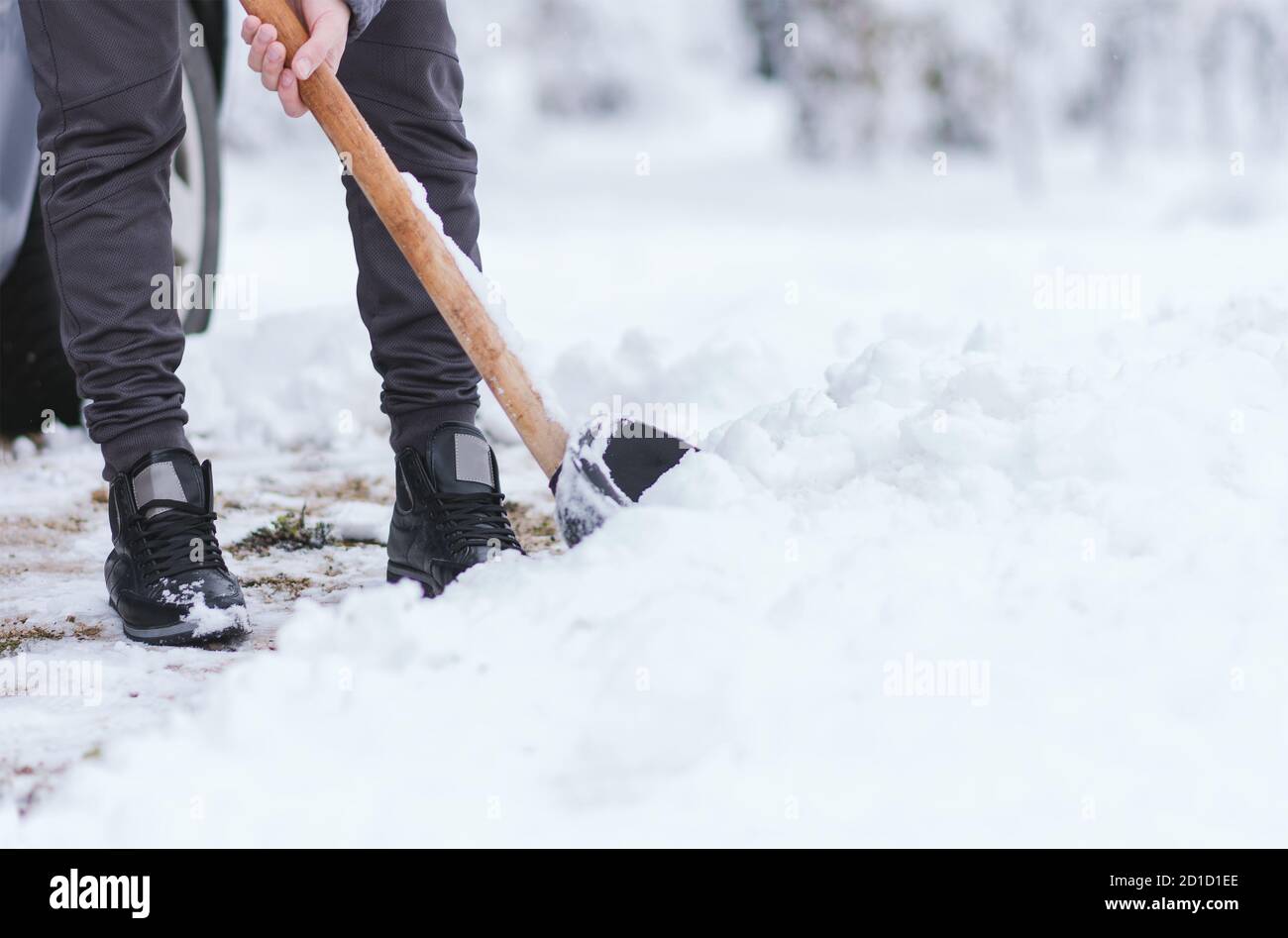 Giovane uomo che pulisce la neve in cortile. Freddo nevoso giorno d'inverno. Vista ravvicinata su gambe e pala. Foto Stock