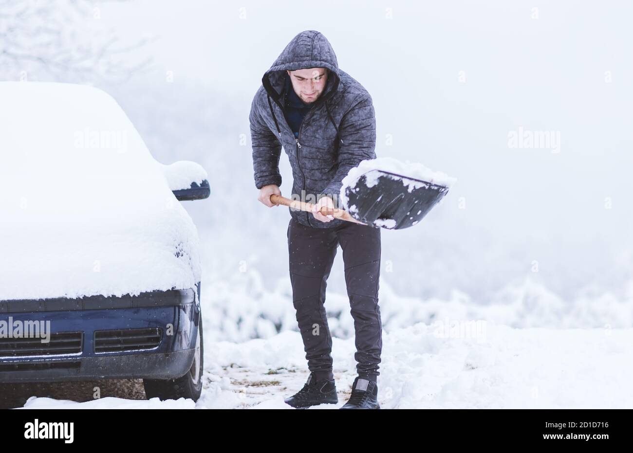 Uomo vestito di giacca che pulisce la neve intorno alla sua auto. Abrogazione per i viaggi. Foto Stock