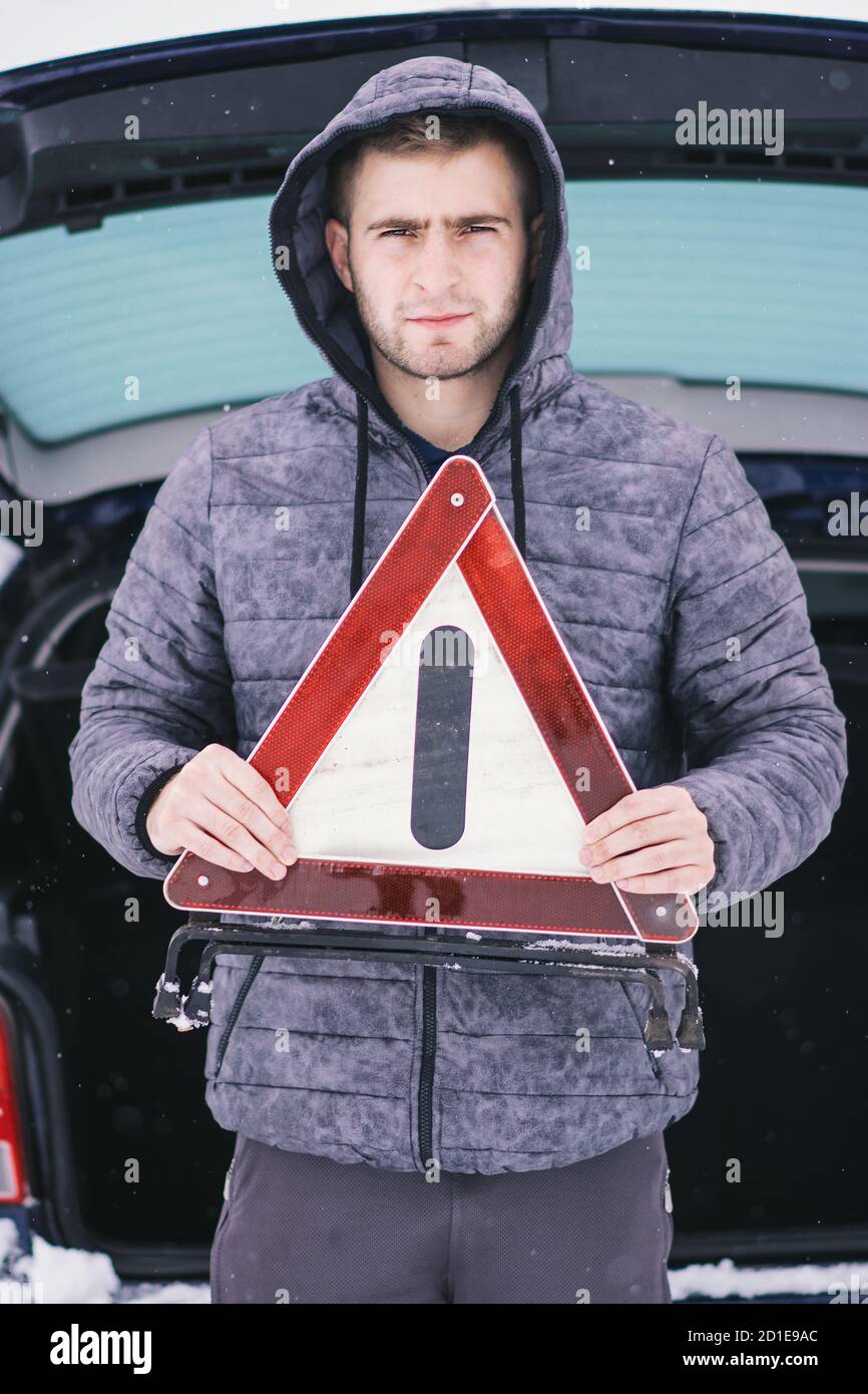 Uomo che tiene un triangolo di sicurezza davanti al bagaglio della sua auto danneggiata. Foto Stock