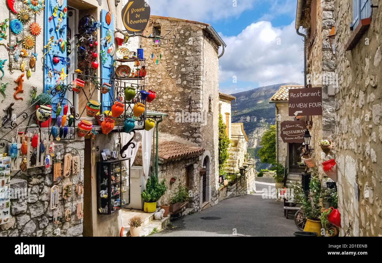 Una pittoresca strada colorata che vende regali e souvenir nel villaggio medievale fortificato di Gourdon, Francia. Foto Stock