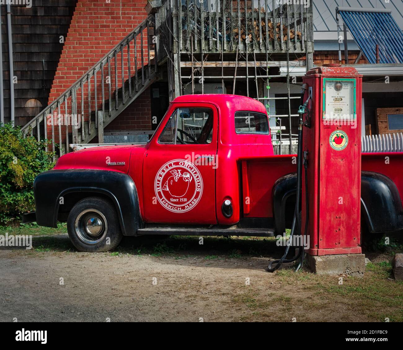 Il servizio di prelievo dal rosso d'epoca è parcheggiato di fronte a una pompa a gas d'epoca in un frutteto di mele del New England per il divertimento dei visitatori. Il logo del frutteto è impr Foto Stock