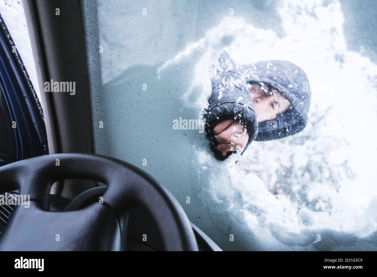 Uomo all'aperto che pulisce la neve sulla sua auto parabrezza.Vista dall'interno dell'auto. Foto Stock