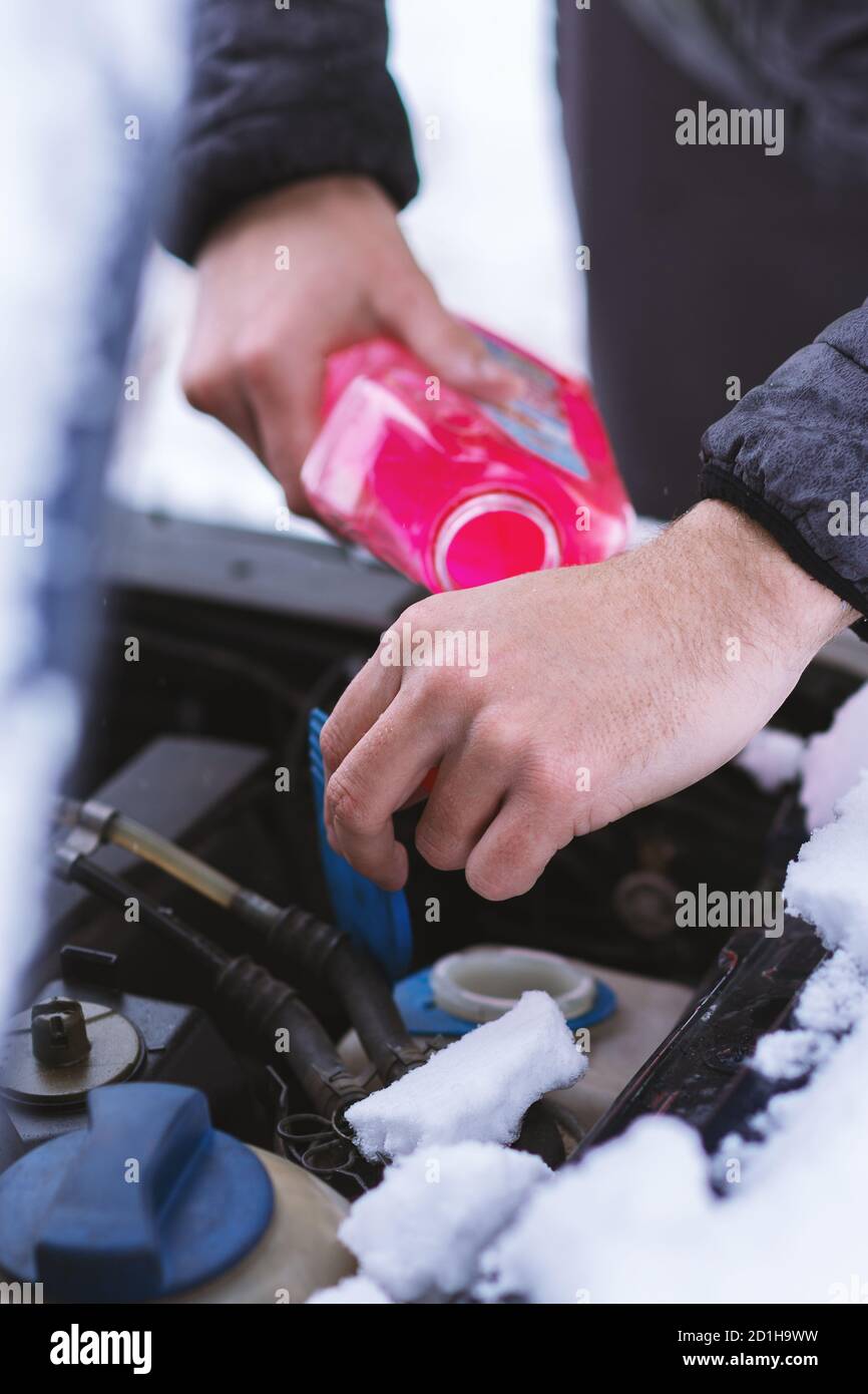 Vista ravvicinata delle mani con la bottiglia che versa liquido di raffreddamento antigelo al motore dell'auto in una fredda giornata invernale. Foto Stock