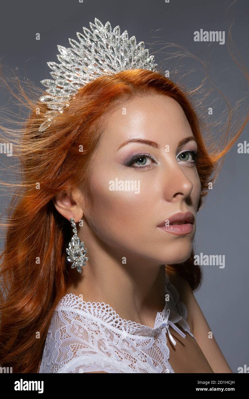 Beauty Queen. Donna nel profilo che tiene la corona diamantata sulla testa e abito in pizzo bianco che guarda su un lato in posa su sfondo grigio isolato. Multiculturale CA Foto Stock