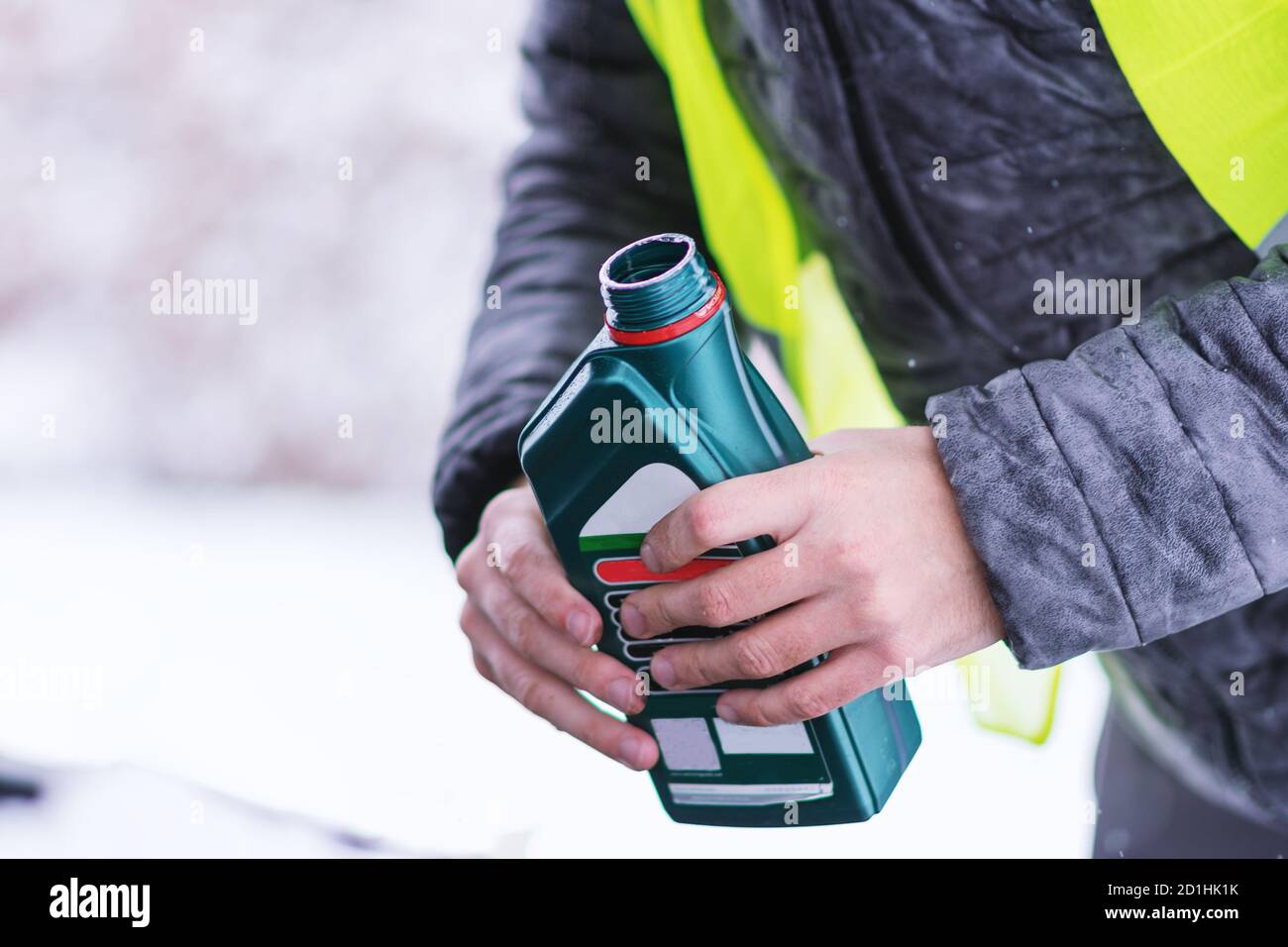 Vista ravvicinata delle mani con la bottiglia che versa l'olio motore al motore dell'auto durante la fredda giornata invernale. Foto Stock