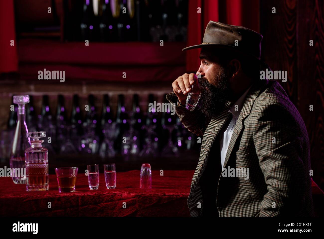 Uomo lavoratore vintage con barba lunga che tiene il whiskey. Seduto al bar. Foto Stock