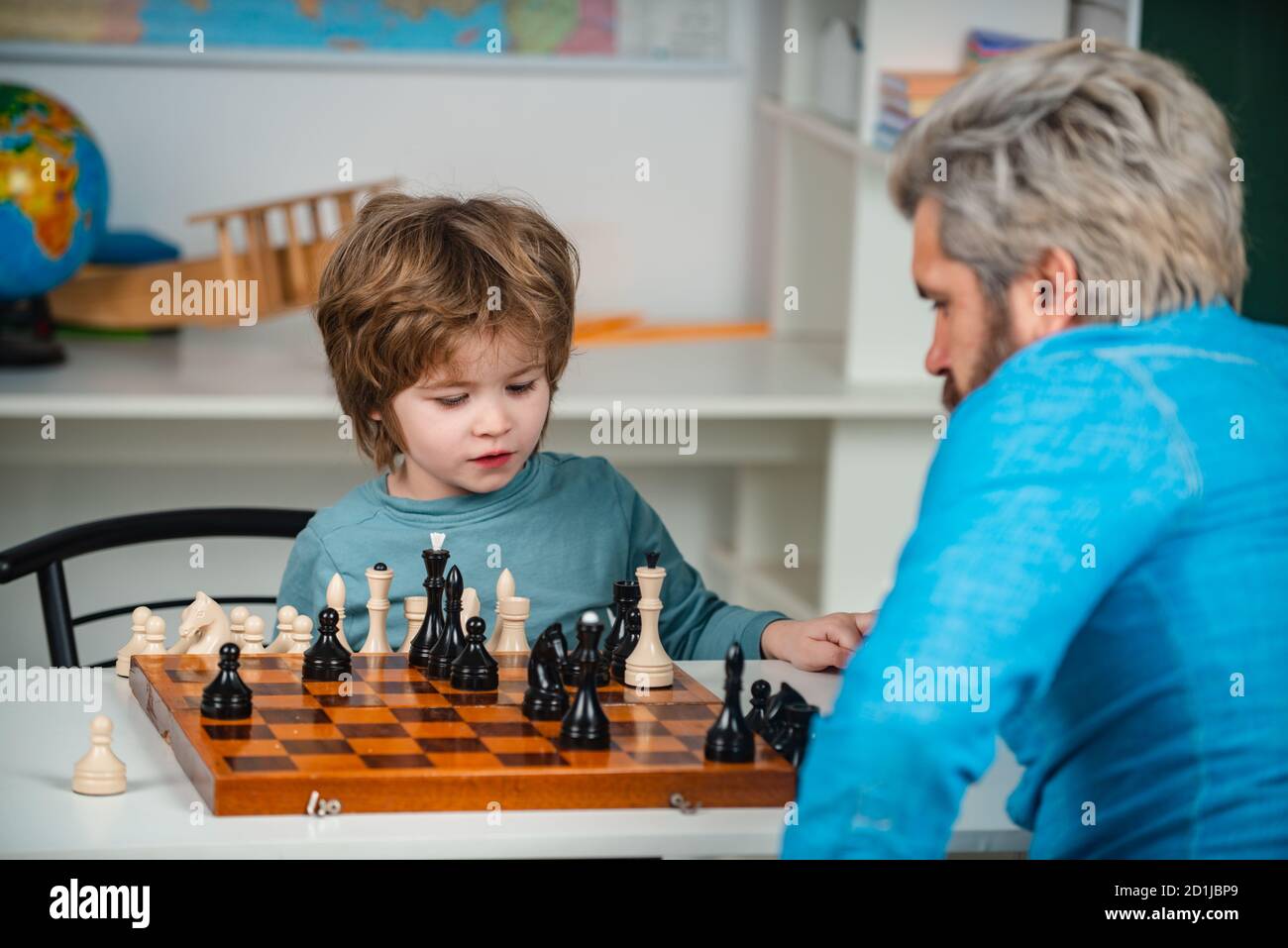 Carino ragazzino che gioca a scacchi con i genitori. Bel maestro che dà lezioni private di scacchi al ragazzo prescolare. Giochi educativi. Foto Stock