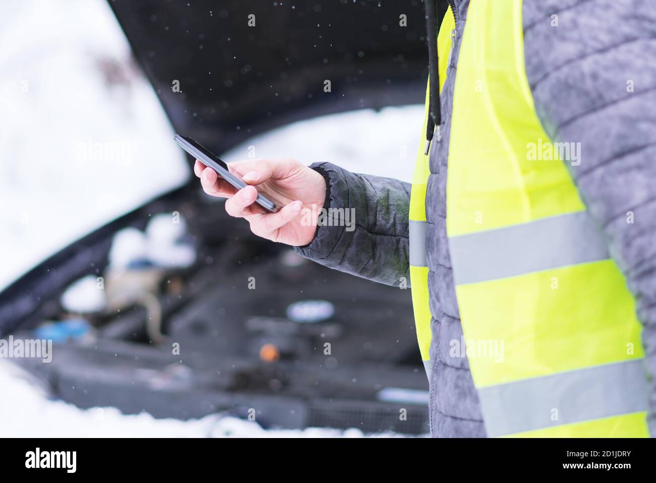 Vista ravvicinata. Uomo che tiene il telefono cellulare e che chiama i servizi di auto invernali per aiutare. Foto Stock