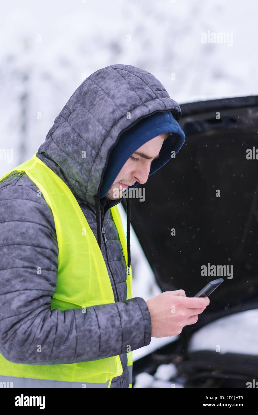 Uomo vestito con giubbotto di sicurezza verde neon che chiama i servizi di auto invernali per aiutare. Foto Stock