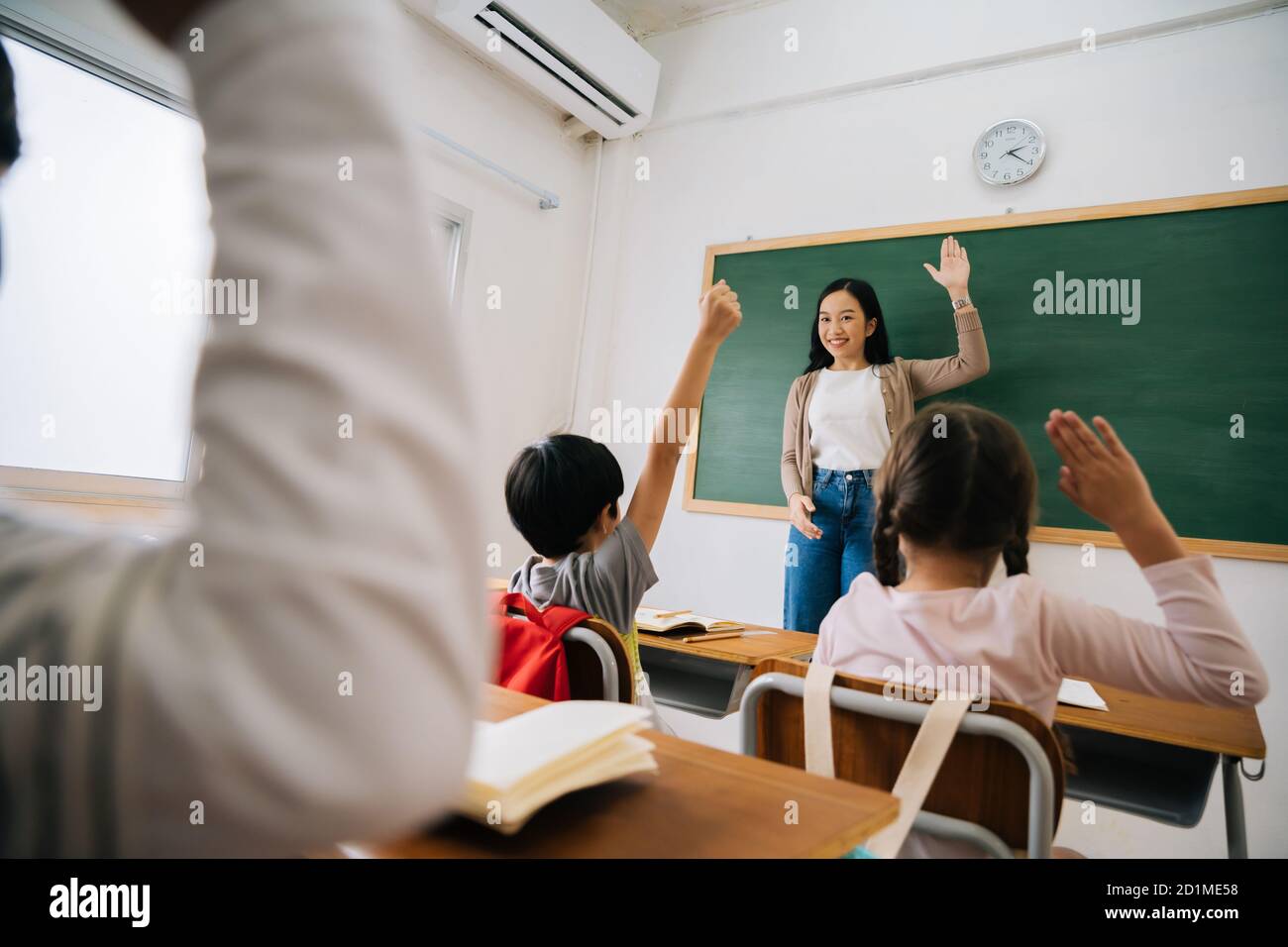 Insegnante di scuola asiatica con studenti che alzano le mani. Giovane donna che lavora a scuola con braccio sollevato, bambini della scuola mettendo le mani in su per rispondere alla domanda, entusiasmo, desideroso, godimento. Foto Stock