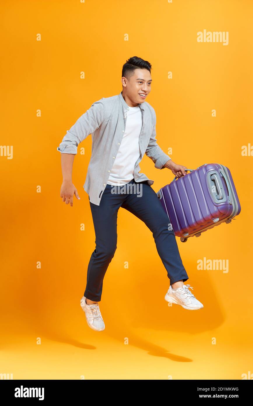 Attraente giovane turista asiatico con biglietto aereo e. passaporto in mano saltando isolato su sfondo giallo studio Foto Stock