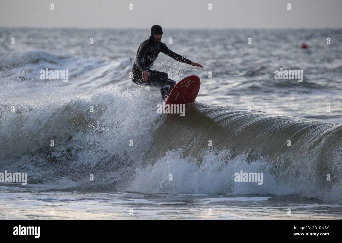 Un surfista corre un'onda nel mare al largo della spiaggia di Boscombe in Dorset. Foto Stock