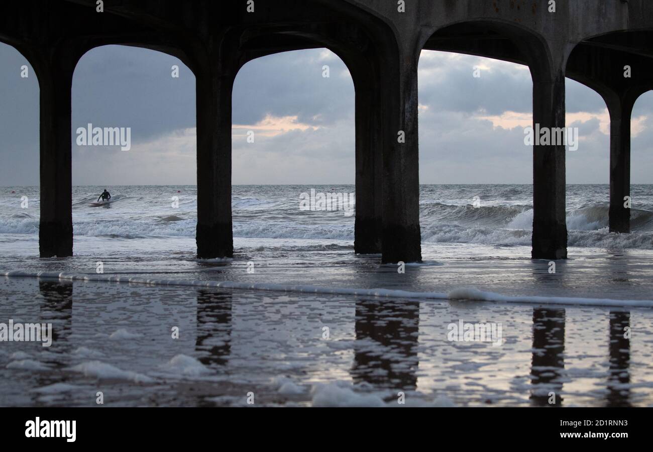 Un surfista corre un'onda nel mare al largo della spiaggia di Boscombe in Dorset. Foto Stock