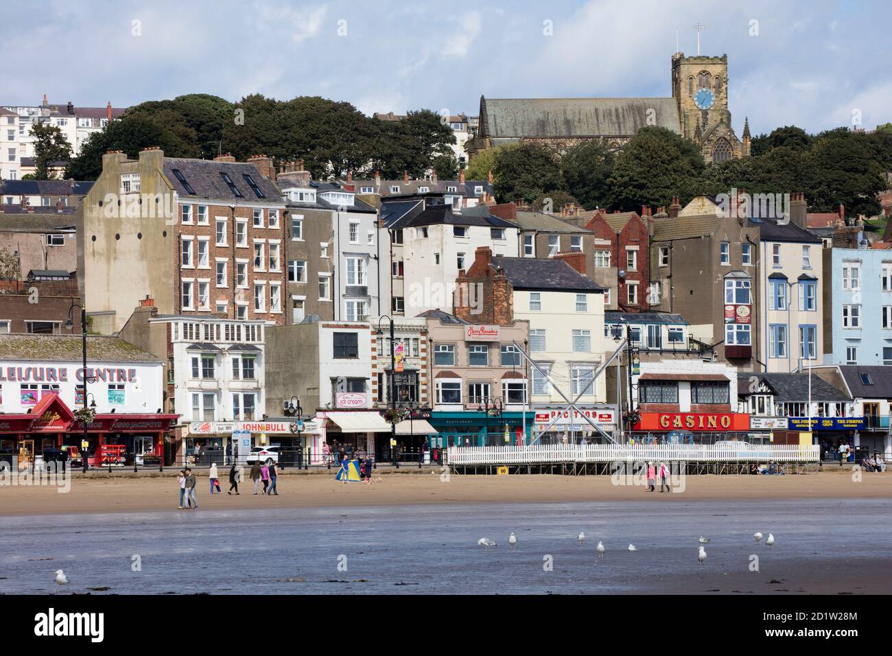 Vista generale che guarda a nord-ovest dalla spiaggia verso negozi, caffetterie e gallerie di divertimento all'estremità nord della strada, con la chiesa di St Mary sullo sfondo, Scarborough, North Yorkshire, Regno Unito. Foto Stock Vista generale che guarda a nord-ovest dalla spiaggia verso negozi, caffetterie e gallerie di divertimento all'estremità nord della strada, con la chiesa di St Mary sullo sfondo, Scarborough, North Yorkshire, Regno Unito. Foto Stock