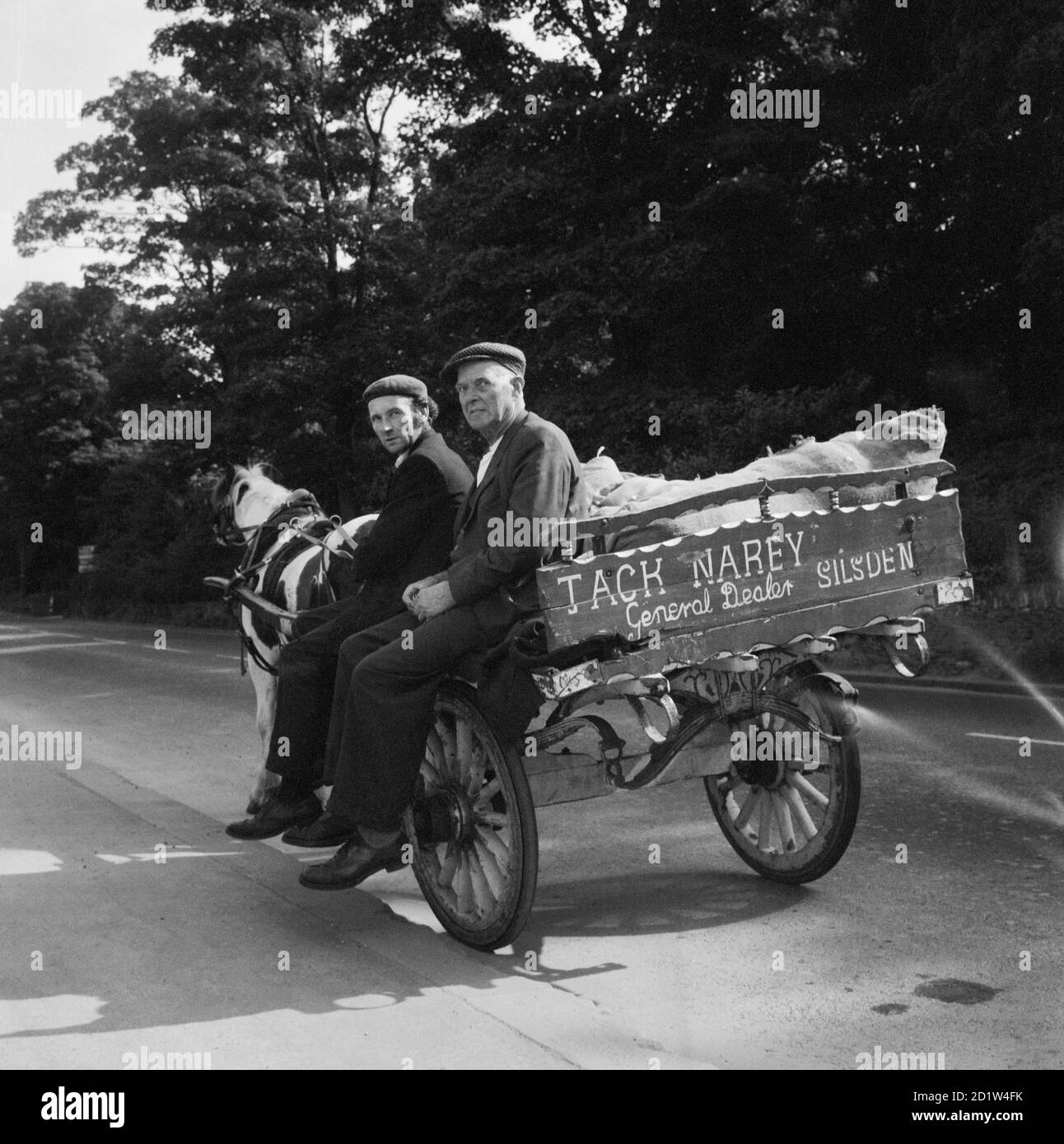 Vista di due uomini che viaggiano lungo una strada nel carro trainato da cavalli di Jack Narey, General Dealer, Silsden, Bradford, West Yorkshire, Regno Unito. Foto Stock