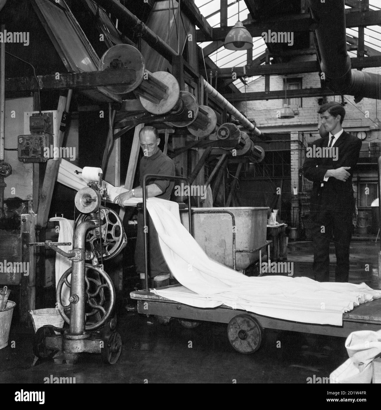 Uomo che indossa vestito in piedi in un mulino, guardando lavoratore a telaio. Foto Stock