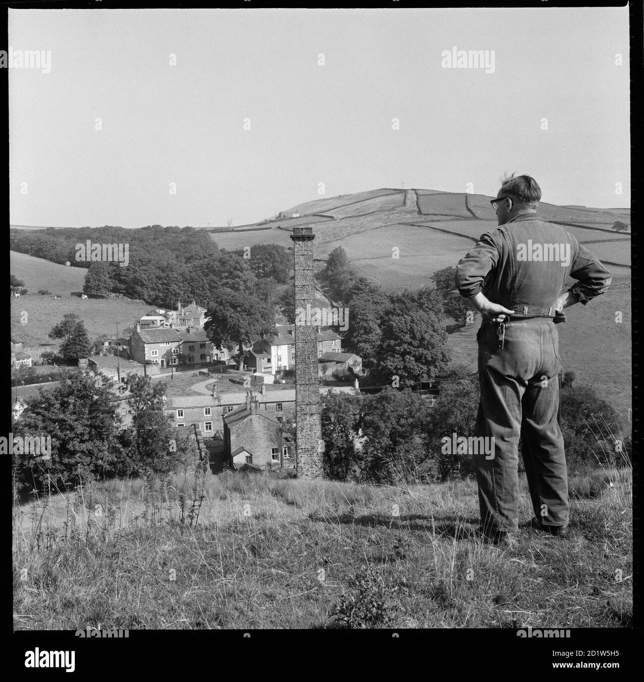 Un uomo che indossa un abito da caldaia in piedi sulla collina a sud-ovest di Dale End Mill, Lothersdale, Craven, North Yorkshire, Regno Unito. Foto Stock