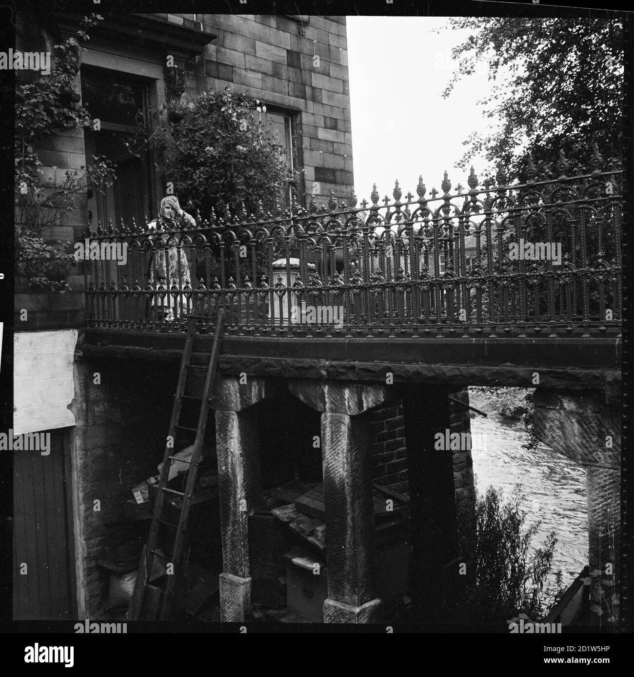 Una donna in piedi sul ponte pedonale che collega la casa al 6 Ireland Bridge alla carreggiata, Bingley, Bradford, West Yorkshire, Regno Unito. Foto Stock