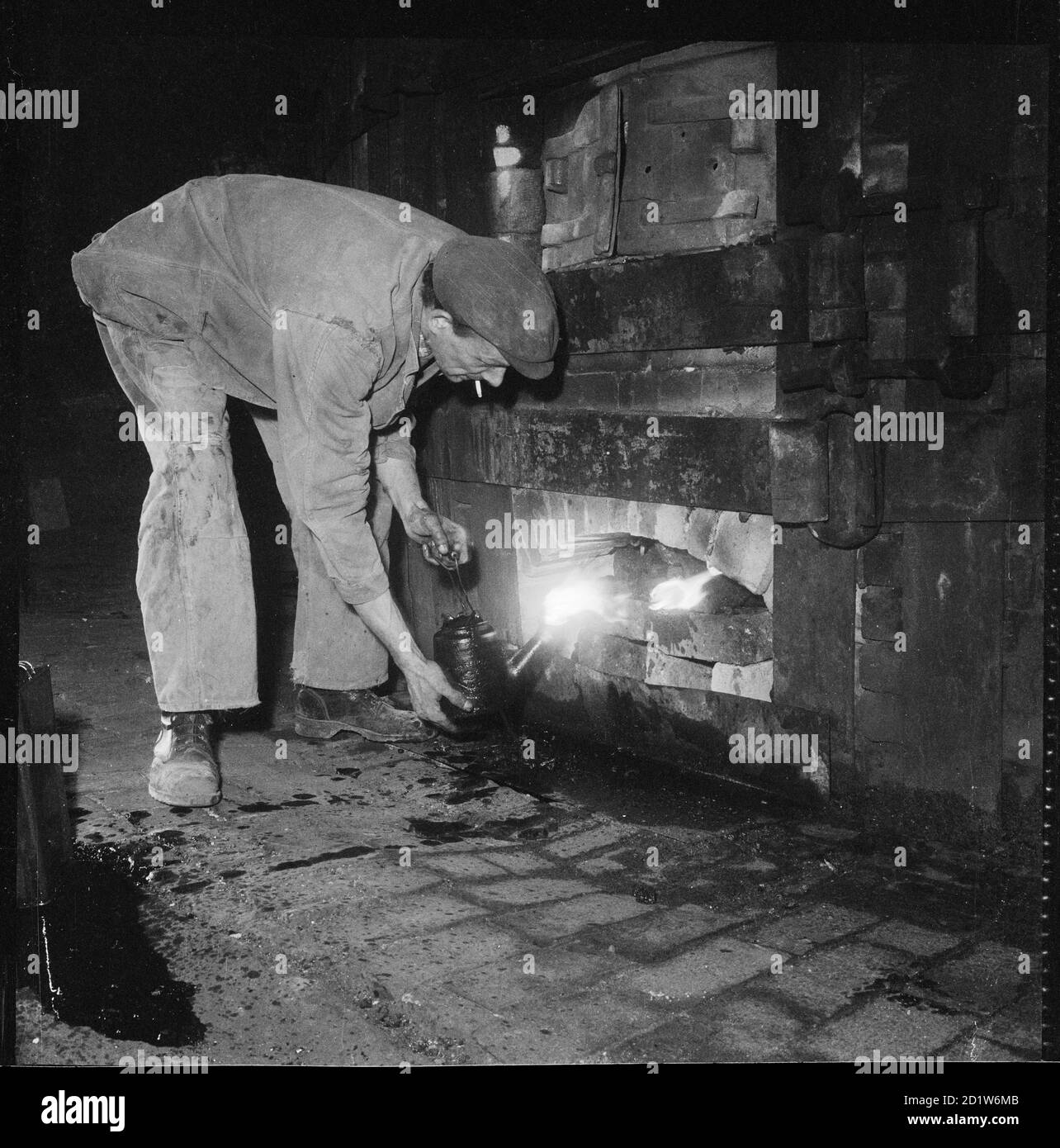 Un uomo che tende il fuoco sotto un forno ad un lavoro di ceramica non identificato, Stoke-on-Trent, Staffordshire, Regno Unito. Foto Stock