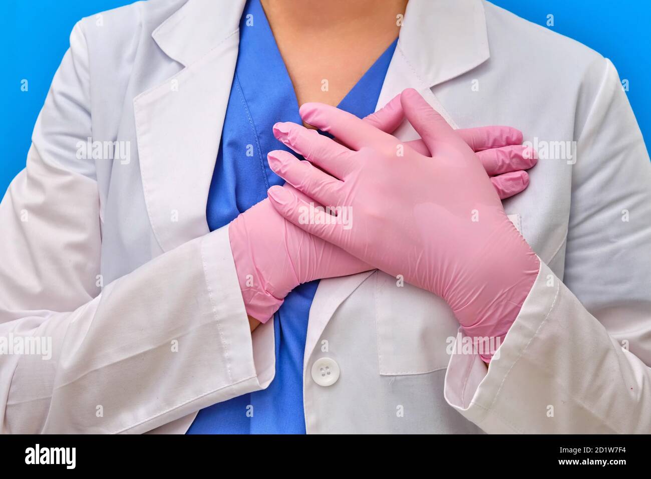 Le mani del medico sono ripiegate sul cuore. Infermiere in guanti protettivi rosa, primo piano. Concetto rimanere a casa fino alla fine dell'isolamento a causa di c Foto Stock