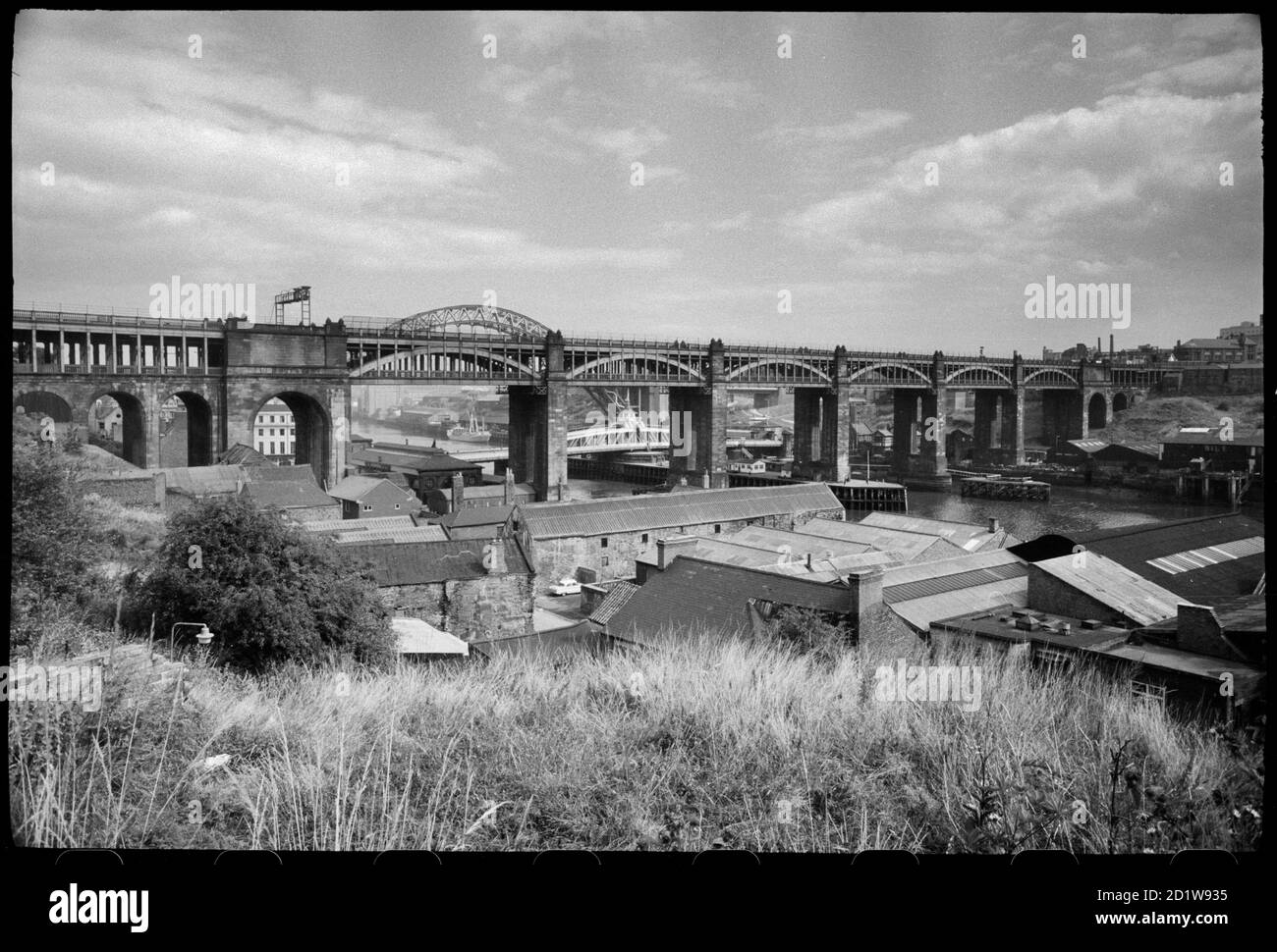 Vista del ponte ad alto livello, un ponte combinato stradale e ferroviario, che attraversa il fiume Tyne, con edifici domestici e industriali in primo piano, e una vista sulla riva sud del fiume sullo sfondo, visto da nord-ovest del ponte, in un'alta vista. Foto Stock