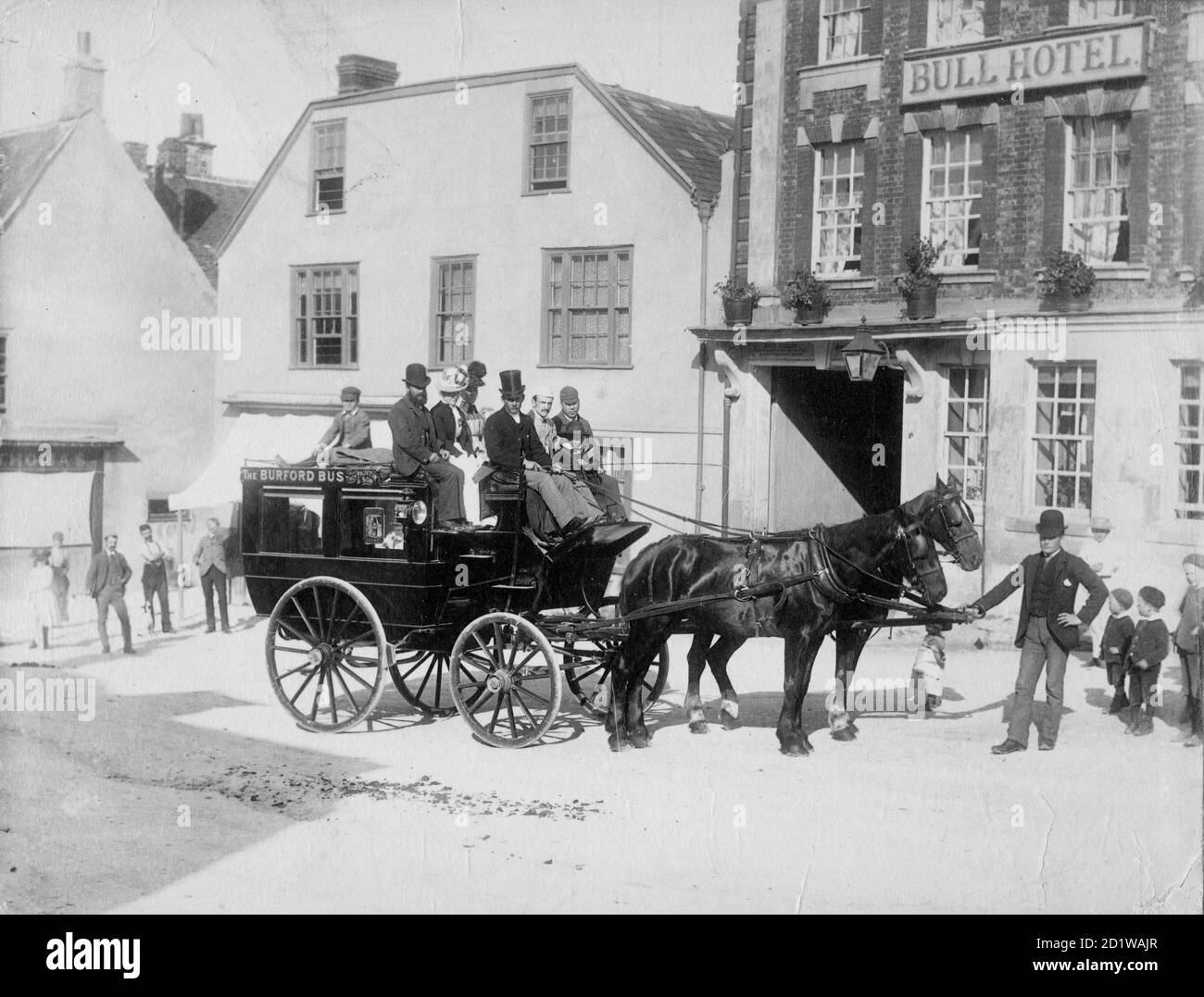 High Street, Burford, West Oxfordshire, Oxfordshire. Un autobus trainato da cavalli e passeggeri che aspettano nella strada fuori dall'hotel, originariamente del XVI secolo, ma con una facciata del XVIII secolo, guardata da bambini locali. Foto Stock