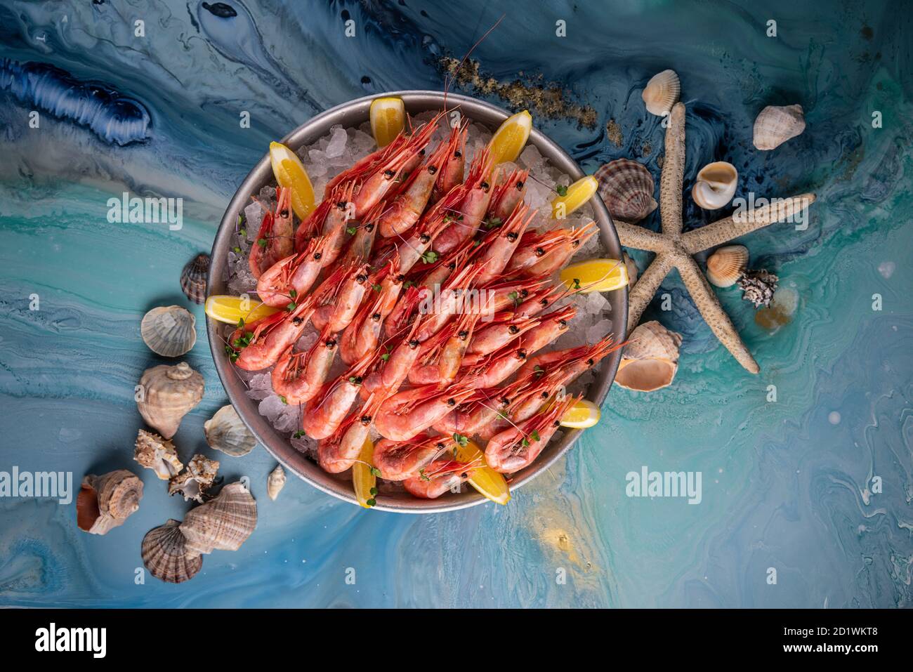 Gamberi rossi in un tondo con ghiaccio e limone. Pronto a mangiare. Menu, vista dall'alto del pesce. Gamberi giganti cotti su sfondo blu. Foto Stock