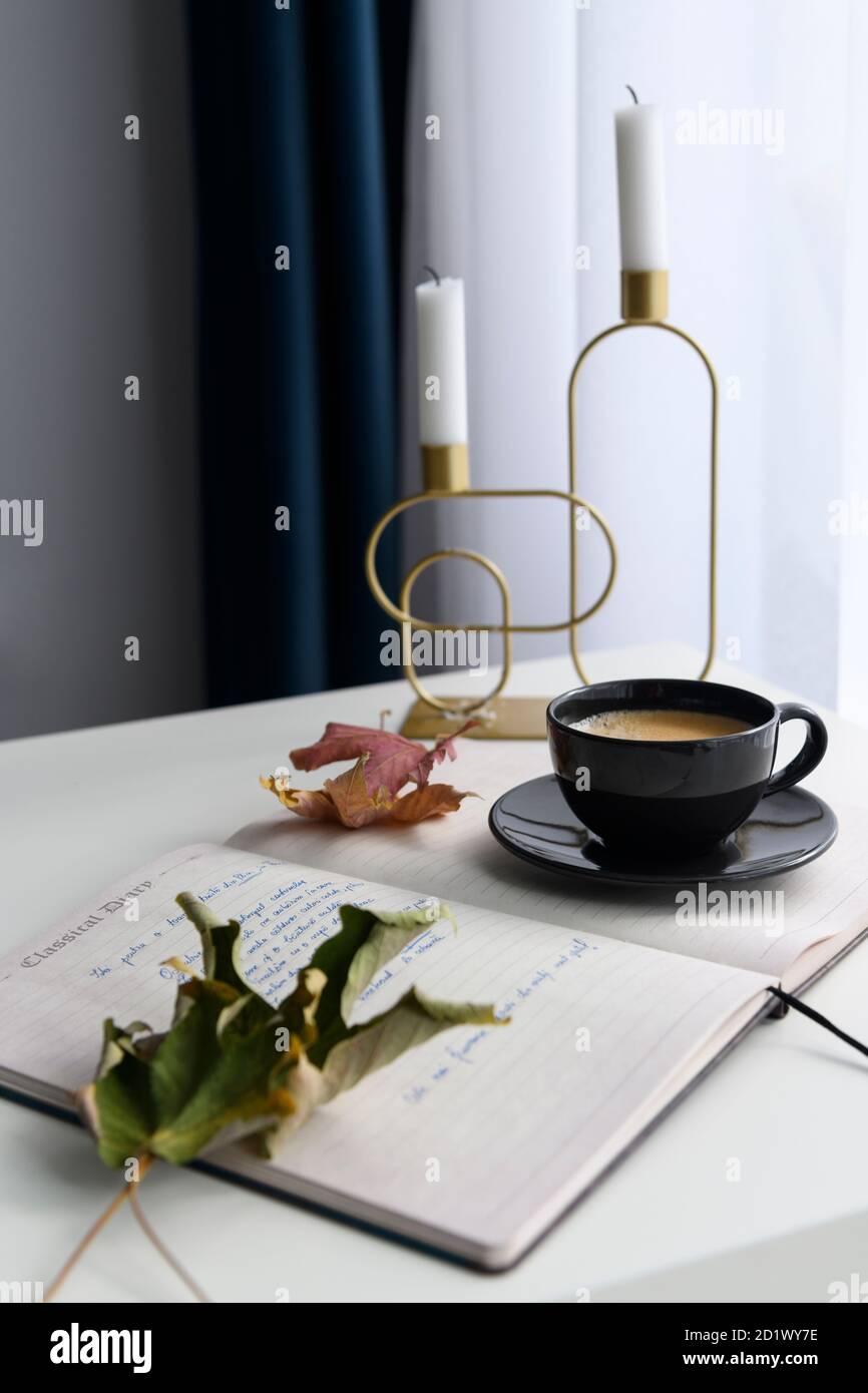 Tazza da caffè, portacandele, notebook e foglie secche in uno scenario autunnale Foto Stock