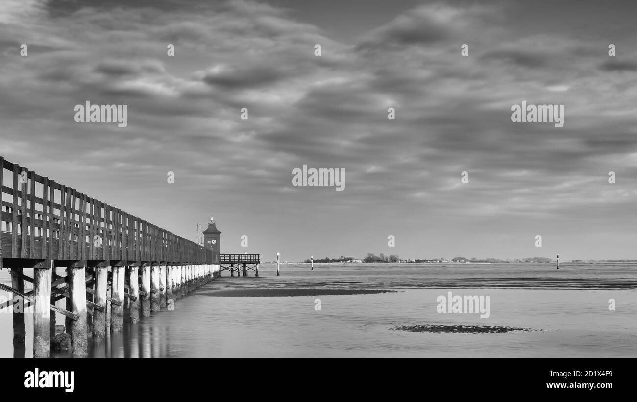 Immagine in bianco e nero di un faro e di un molo in legno sotto un cielo drammatico. Lignano Sabbiadoro, Friuli Venezia Foto Stock