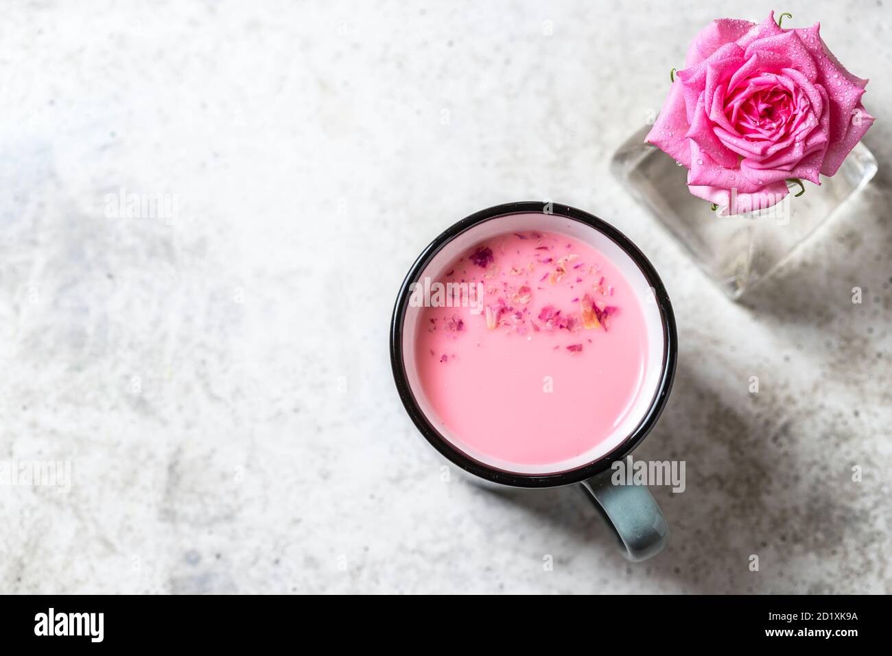 Latte ayurvedico di luna di rosa. Una forma trendy e rilassante di drink prima di letto. Latte con petali di rosa in una tazza grigia su un fondo di cemento chiaro. Foto Stock