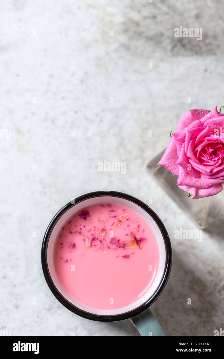 Latte ayurvedico di luna di rosa. Una forma trendy e rilassante di drink prima di letto. Latte con petali di rosa in una tazza grigia su un fondo di cemento chiaro. Foto Stock