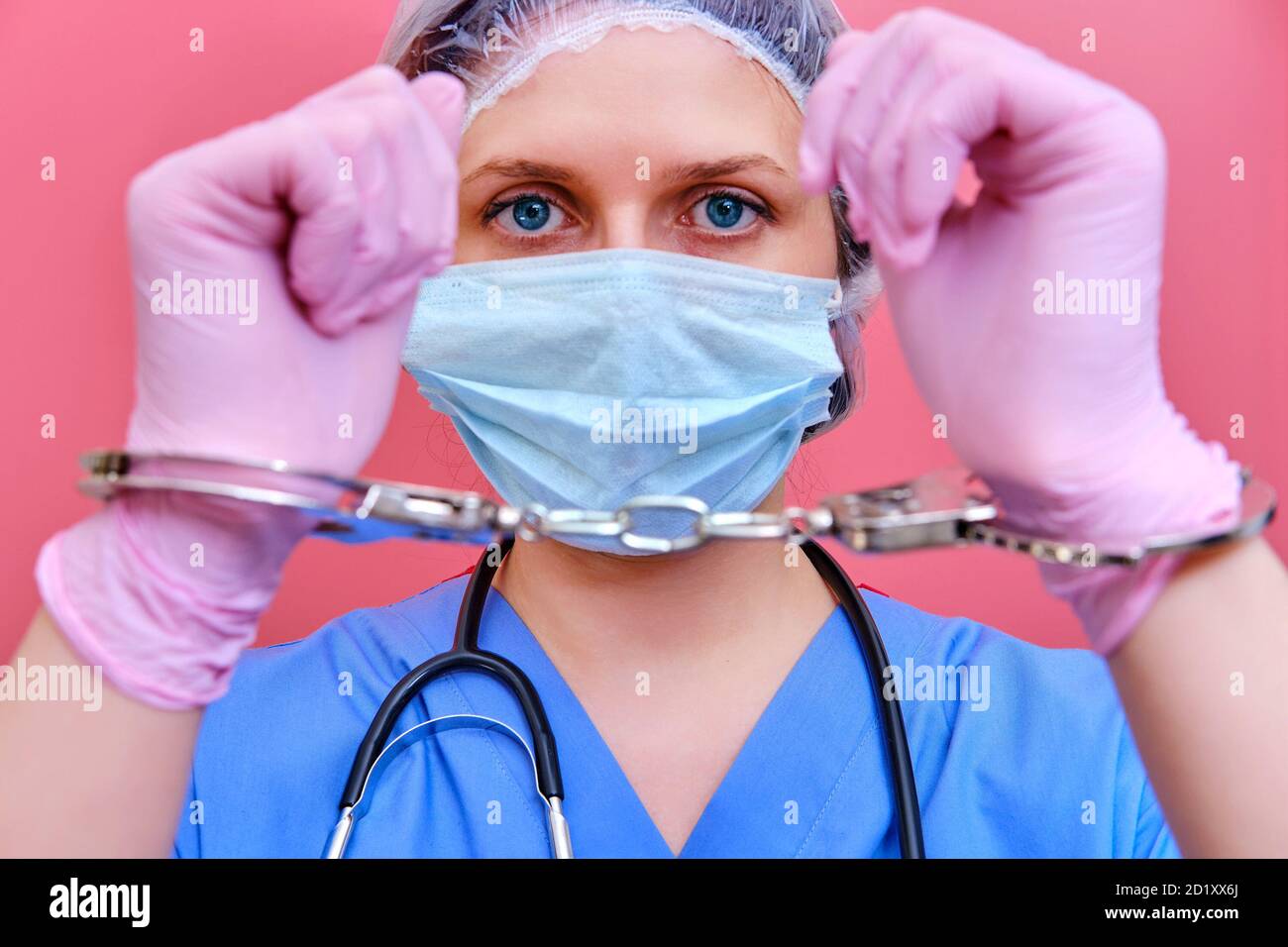 Un'infermiera su sfondo rosa mostra le mani in manette, closeup. Medico arrestato per una tangente da un paziente, concetto Foto Stock