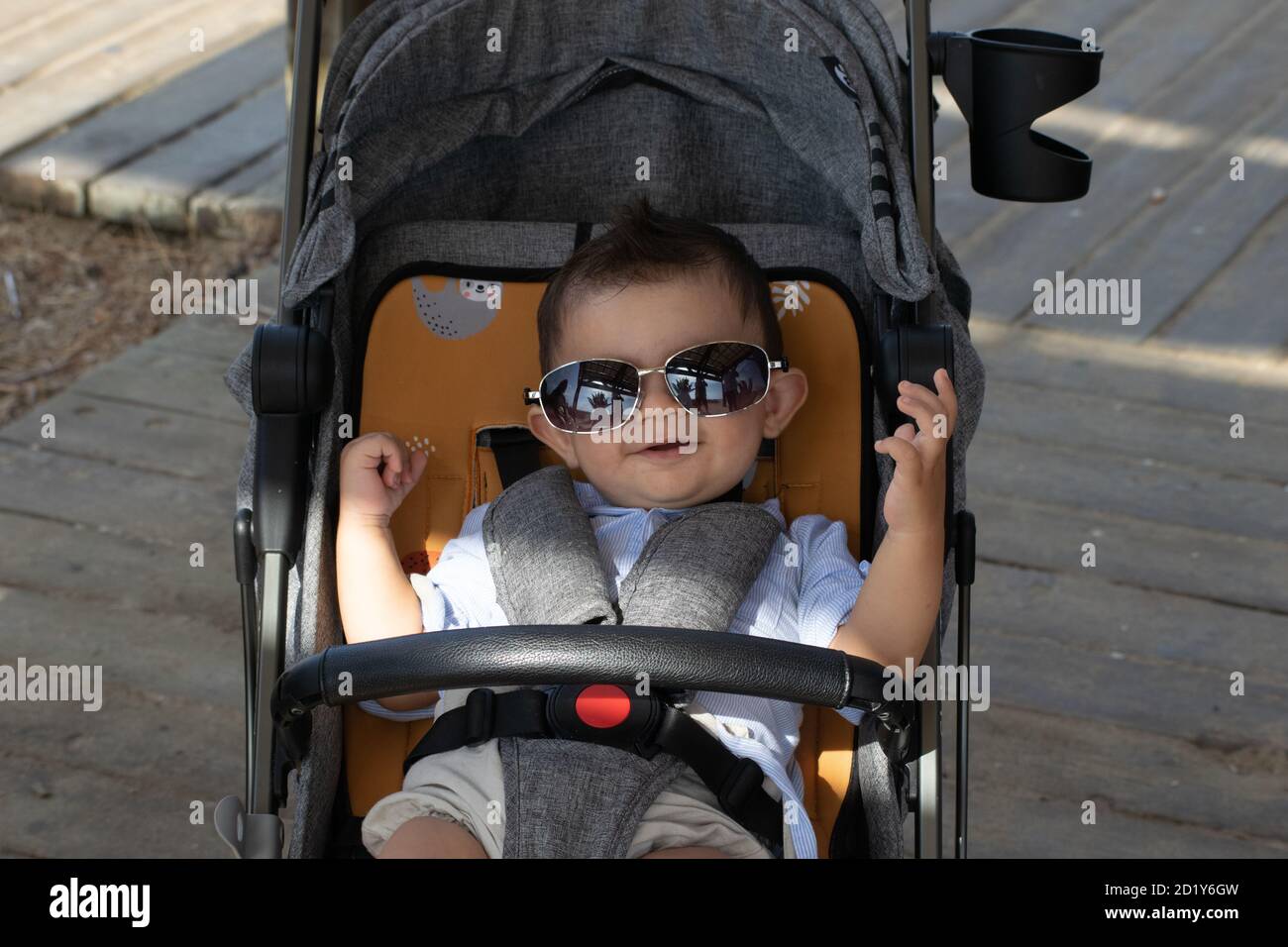 Bambino dolce e divertente che indossa occhiali da sole oversize eleganti seduti in un passeggino Foto Stock