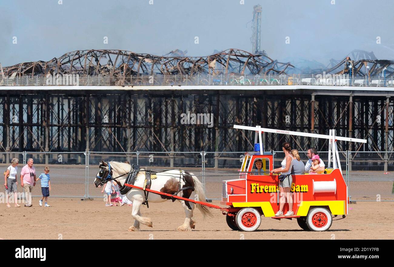 Holiday makers pass the Grand Pier at Weston-Super-Mare in south west England July 28, 2008. Firefighters were called to a large blaze that swept through the historic pier at the Somerset seaside resort of Weston-super-Mare on Monday, police said. Flames and thick black smoke engulfed the structure and could be seen from the M5 motorway, several miles from the coast, a fire brigade spokeswoman said.   REUTERS/Toby Melville    (BRITAIN) Foto Stock