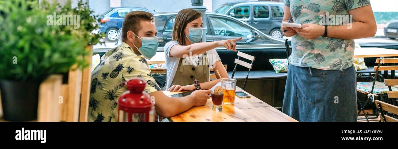 Accoppia con maschera facendo ordine di cibo al cameriere Foto Stock