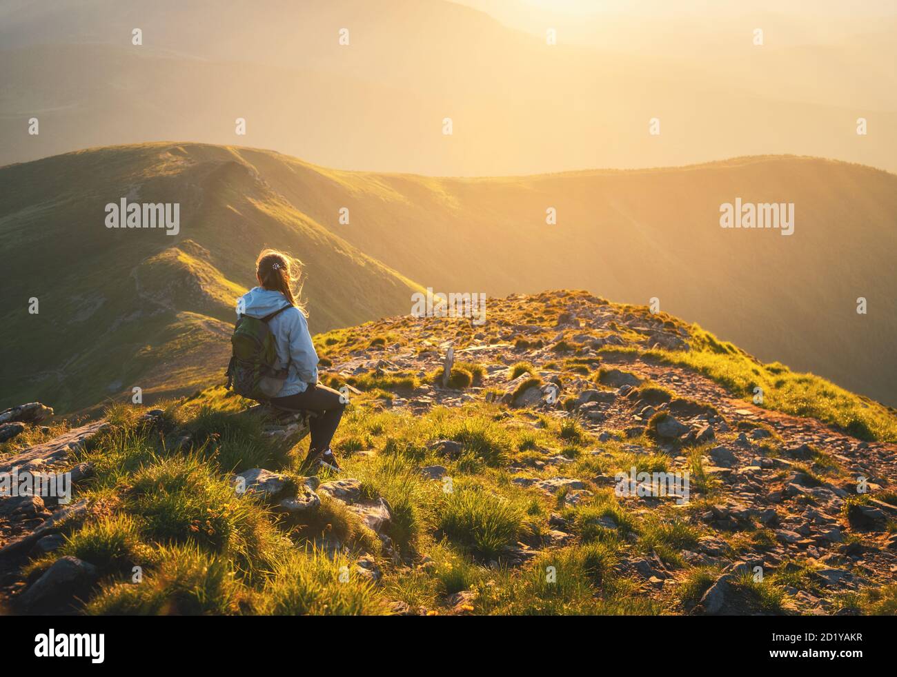 Donna con zaino seduto sulla cima della montagna al tramonto Foto Stock