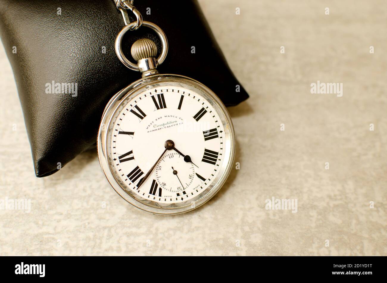 Vecchio orologio tascabile su cuscino nero e sfondo grigio testurizzato. numeri romani che indicano l'ora Foto Stock