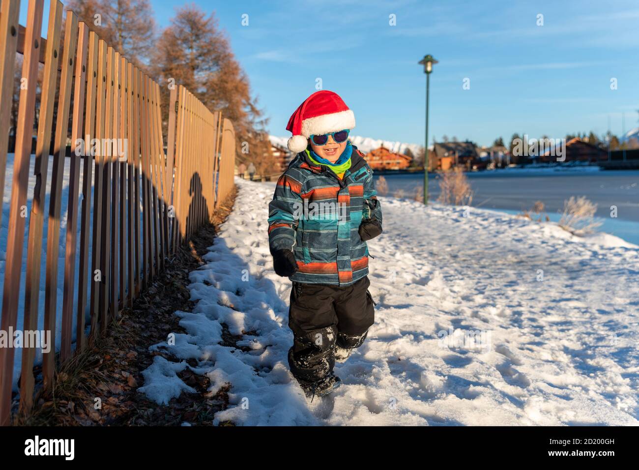 Ragazzo con cappello rosso Babbo Natale su uno sfondo di paesaggio invernale. Felice bambino sorridente che cammina nella neve a Natale. Crans Montana in Svizzera. Foto Stock