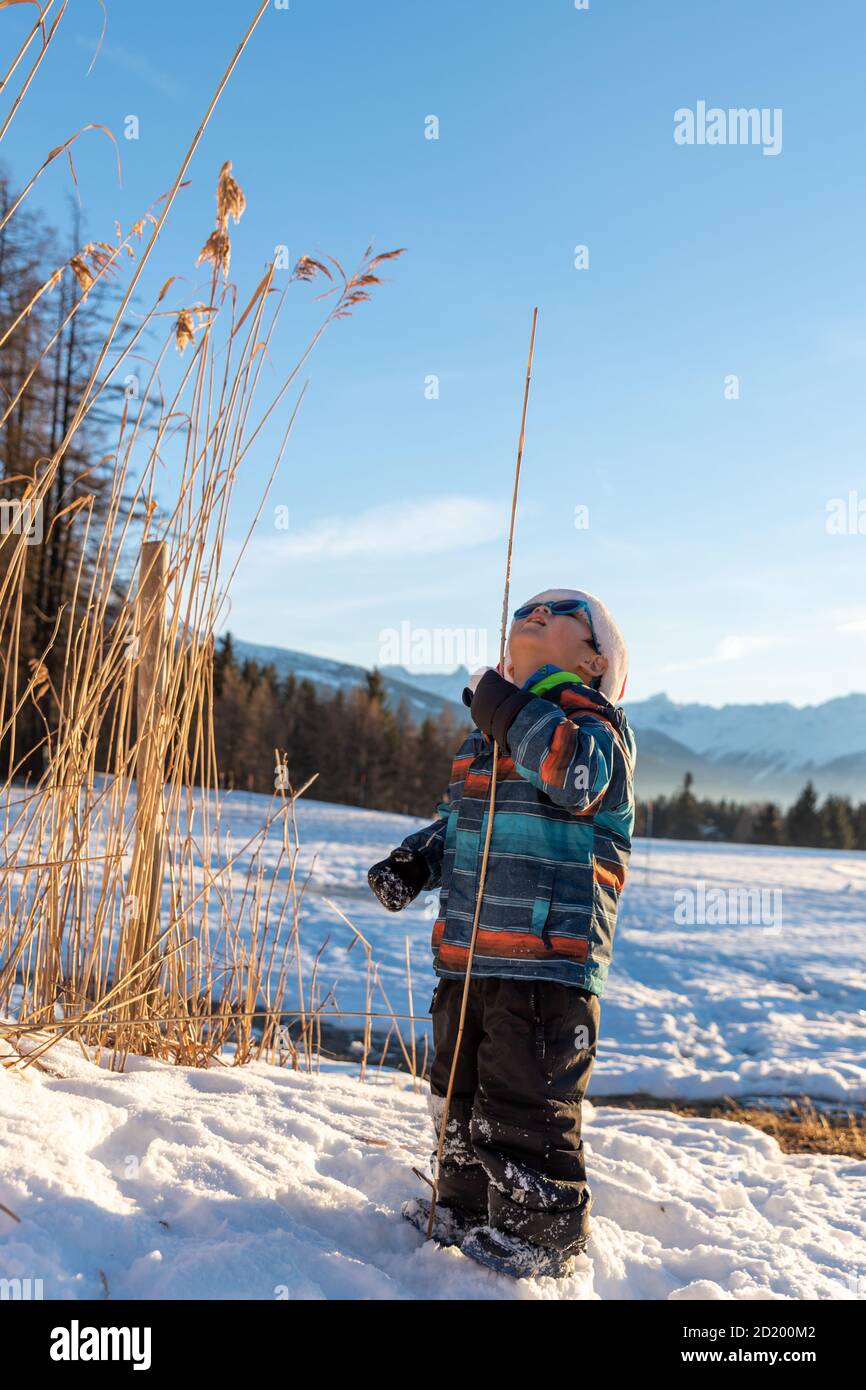 Ragazzo con cappello rosso Babbo Natale su uno sfondo di paesaggio invernale. Bambino sorridente felice nella neve a Natale in piedi accanto a piante alte all'aperto. Gru Foto Stock