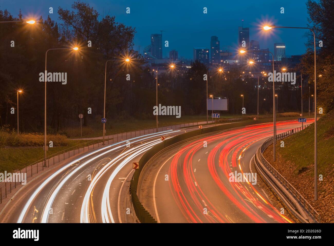 Auto sentieri leggeri su un'autostrada curva per la città di notte. Sentieri per il traffico notturno e paesaggi urbani. Strada urbana leggera con movimento dei fari. Foto Stock