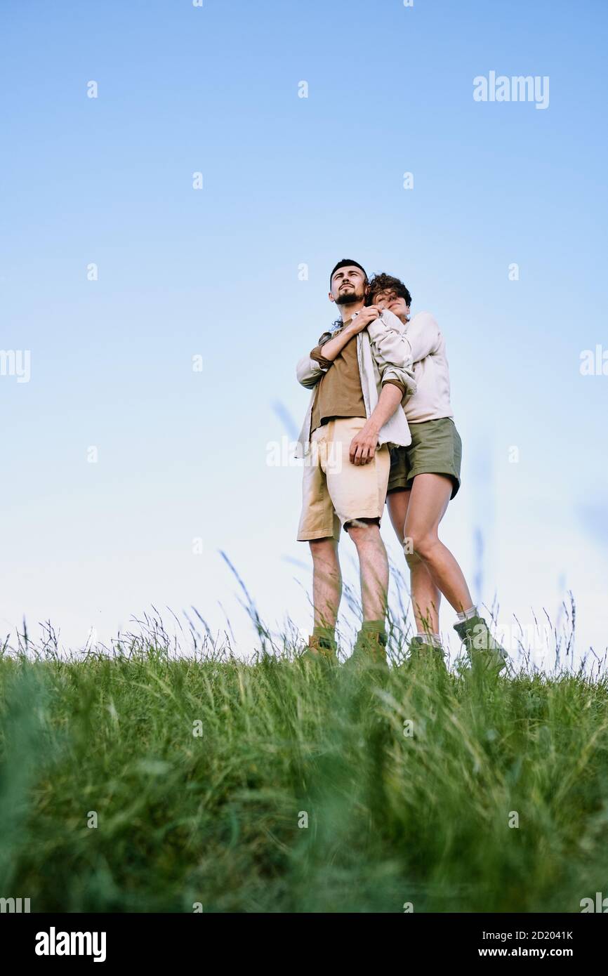 Sotto la vista di serena ragazza abbracciando giovane ragazzo mentre loro godendo la bellezza del paesaggio di campagna insieme Foto Stock