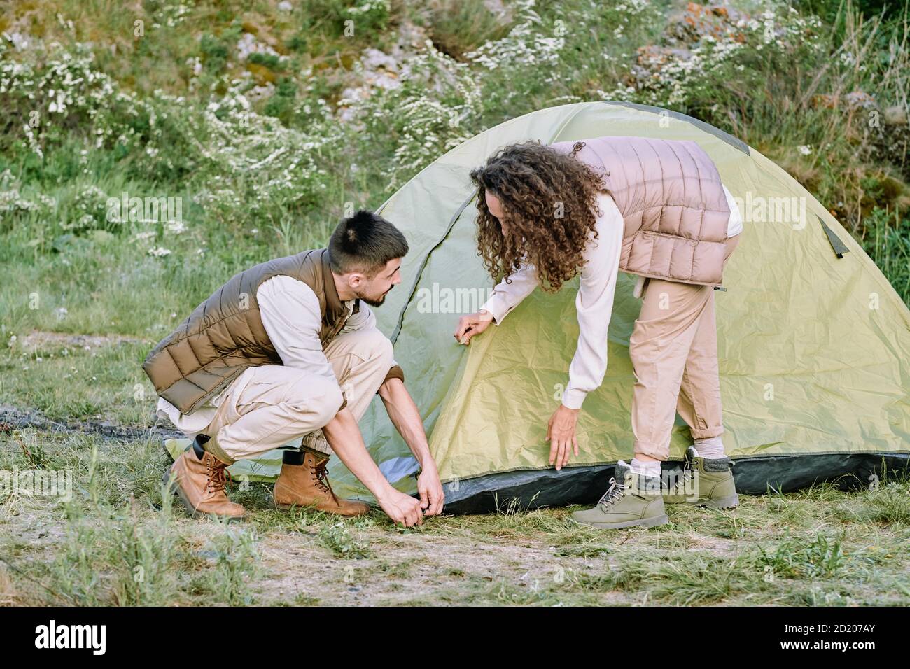 Bella giovane coppia in giubbotti di messa a punto tenda durante la preparazione per il campeggio all'aperto Foto Stock