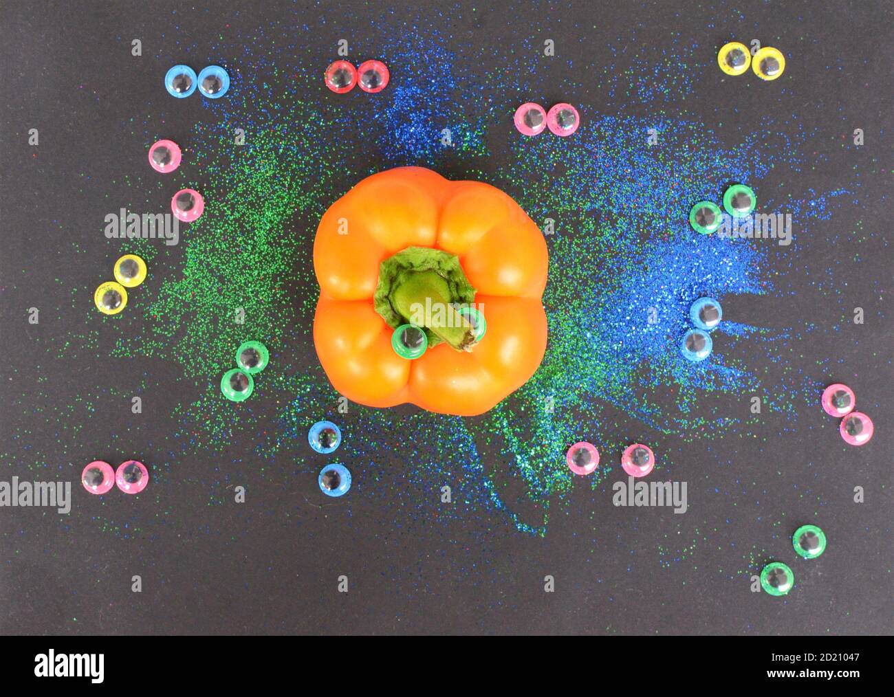 Divertente concetto creativo di Halloween: Un peperoncino arancione e colorati occhi di plastica su uno sfondo nero con una rosa Foto Stock