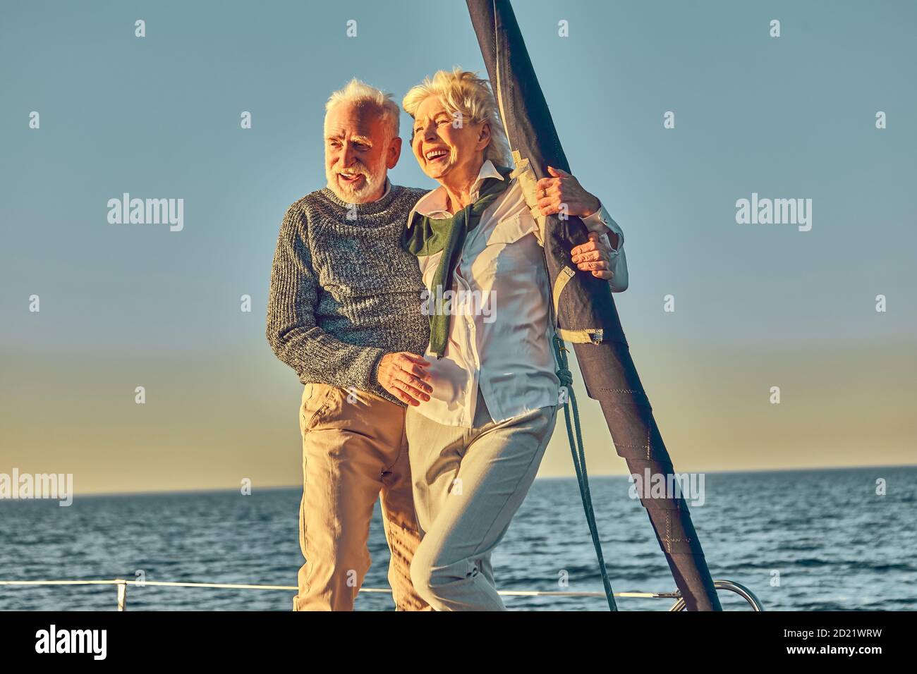 Felice coppia anziana in amore, uomo e donna in pensione in piedi sul lato della barca a vela o yacht ponte che galleggia in mare, godendo incredibile tramonto e. Foto Stock