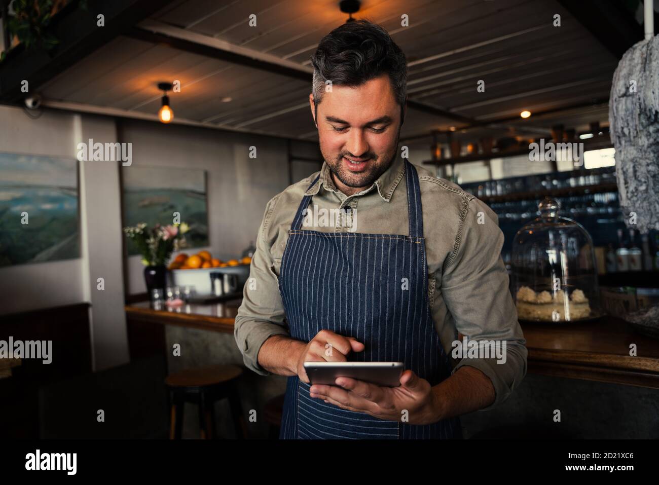 Il proprietario di una caffetteria maschile sorride al tablet mentre si trova nella caffetteria. Foto Stock