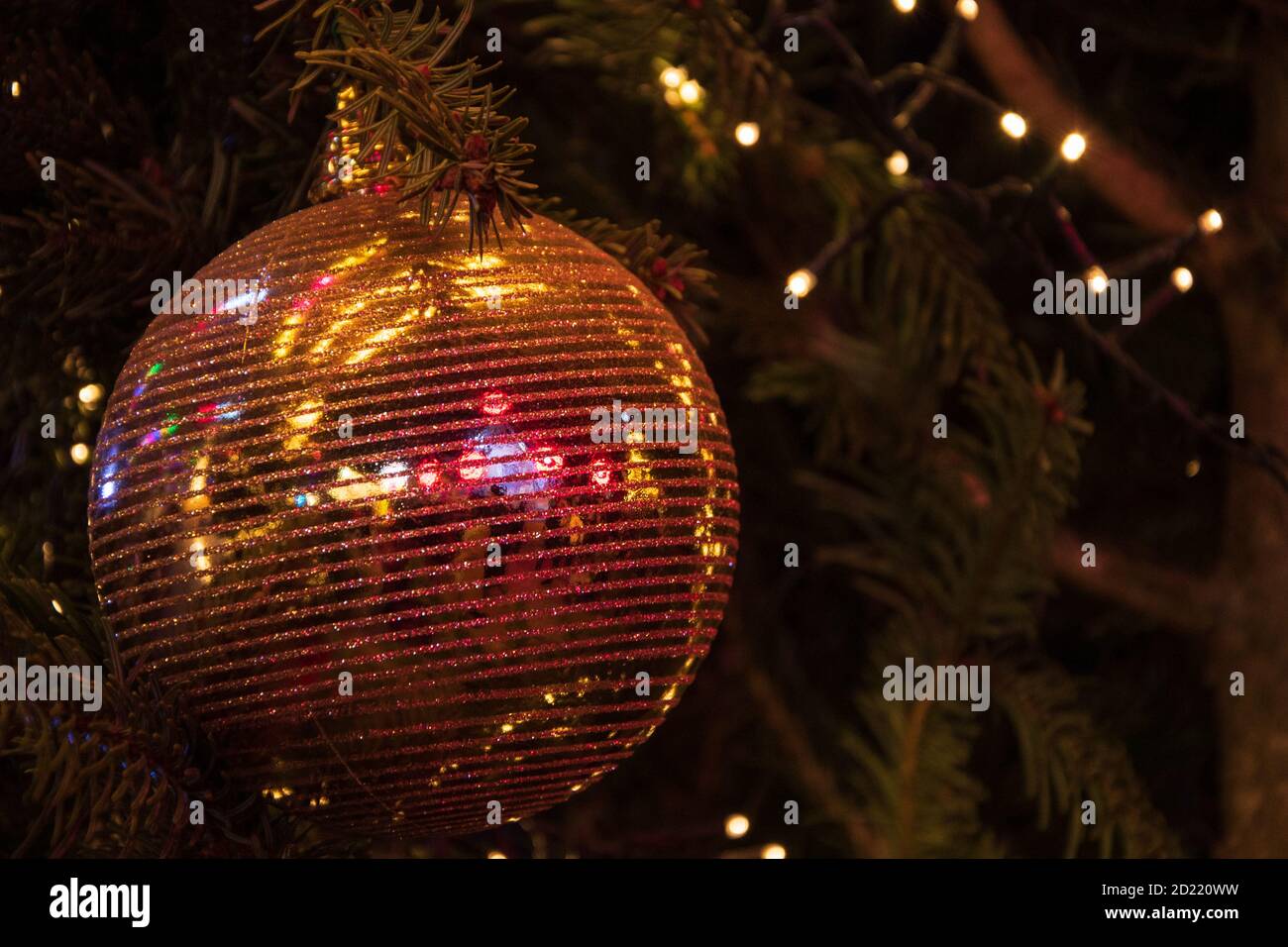 Palla di Natale a righe lucenti sull'albero di Natale e ghirlanda di luci di Natale. Xmas sfondo. Concetto di vacanza invernale. Riflessione. Bokeh. Selettivo fo Foto Stock