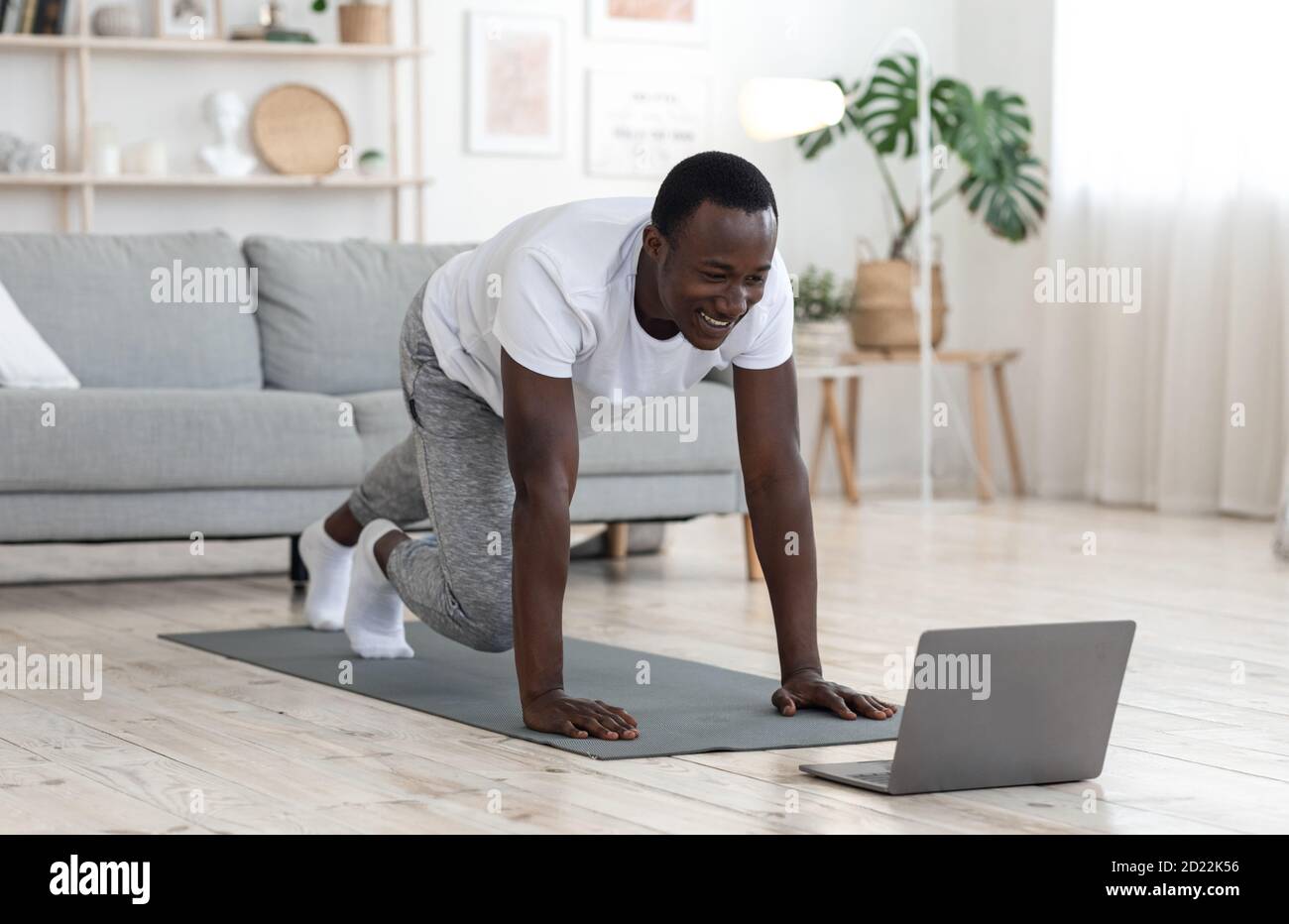 Gioioso ragazzo nero che si esercita a casa, guardando lo schermo del computer portatile Foto Stock