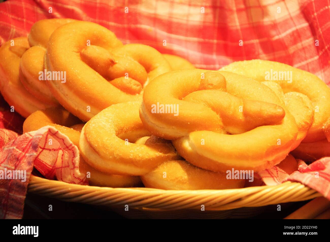 Dolci ciambelle di pretzel su asciugamano a scacchi in cesto di vimini. Selezionato fuoco sul tessuto ritorto. Foto a toni. Foto Stock