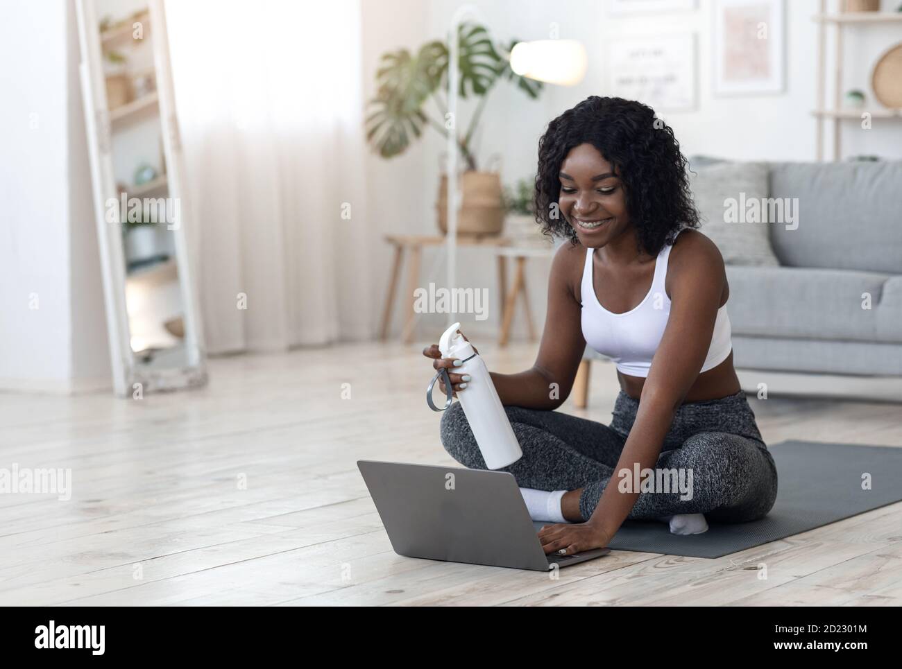 Bella donna africana che si esercita a casa, utilizzando il computer portatile Foto Stock