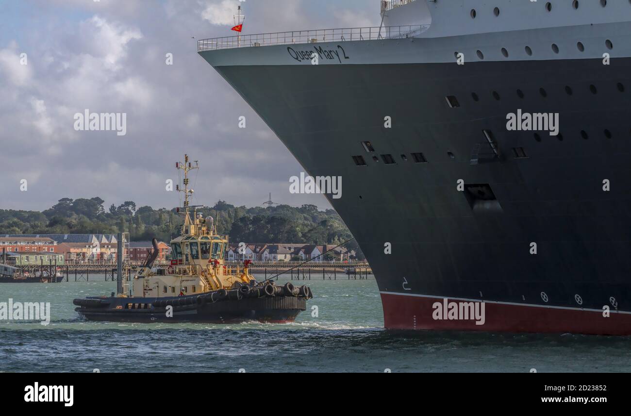 Potente piccolo Tugboat che guida, tirando e trainando la nave da crociera Queen Mary Two via da UN ormeggio mentre si prepara a partire. Southampton Docks Regno Unito Foto Stock
